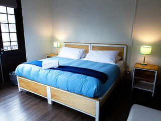 Simple bedroom with a large bed covered in blue bedding, accompanied by minimalist decor.