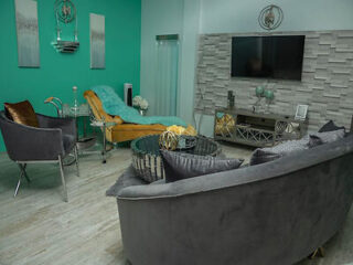 A modern living room with a teal accent wall, gray furniture, and a flat-screen TV mounted on a stone wall