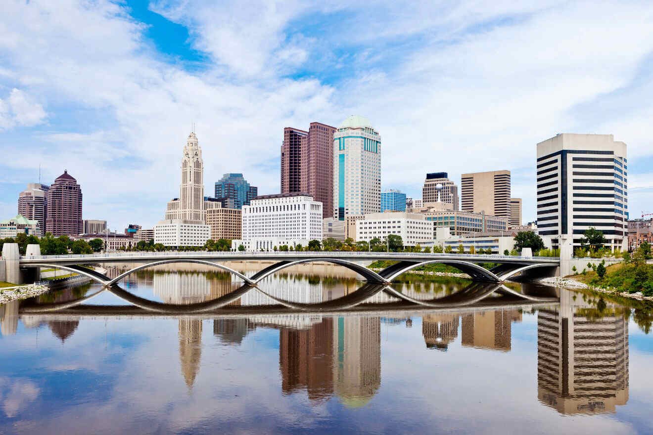 Skyline of a city with several modern buildings, a prominent bridge in the foreground, and a reflective river below.