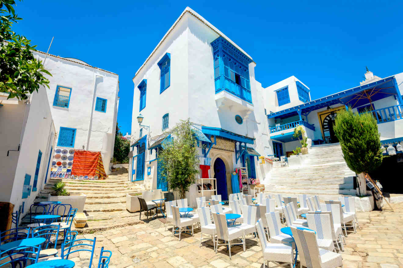 A picturesque courtyard in Sidi Bou Said, with whitewashed buildings adorned with blue shutters, and outdoor seating on cobblestone streets.