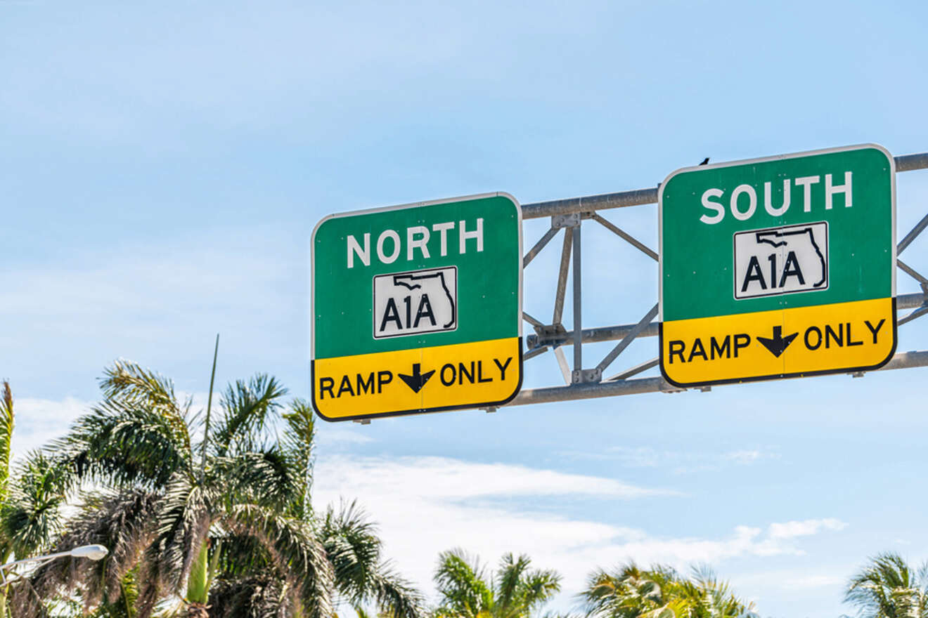 Green highway signs for A1A indicate directions for North and South ramps with palm trees and a clear sky in the background.