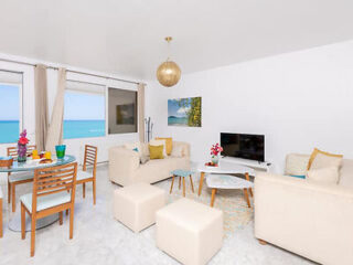 A modern living room with white furniture, ocean views, and a dining area with a glass-top table.