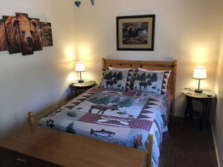 A bedroom with a wooden bed frame, wildlife-themed bedding, two bedside tables with lamps, and bear-themed wall decorations.