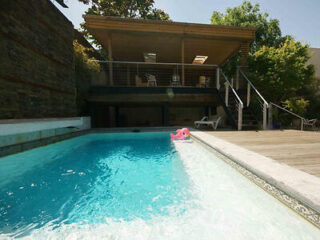 Backyard pool area with a wooden deck and a raised seating area under a shaded structure.