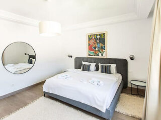 A minimalist bedroom with a large bed, modern decor, and a circular mirror on the wall.