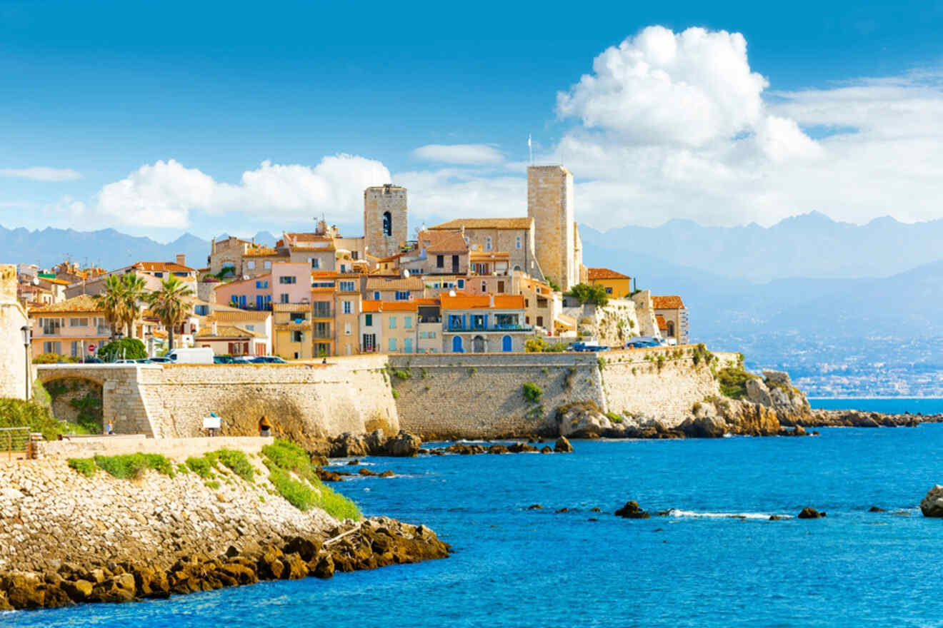 Scenic coastal view of a historic town with stone buildings and towers perched on a cliffside, overlooking a calm blue sea under a clear sky.