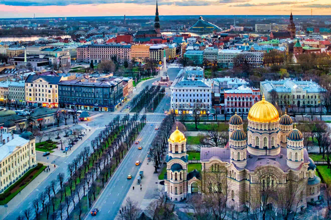 Aerial view of a cityscape featuring a prominent church with golden domes, wide streets, and various buildings in the background under a cloudy sky.