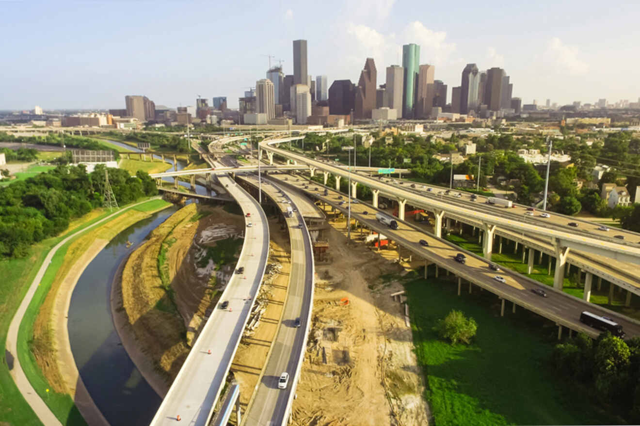 Aerial view of a freeway interchange under construction with multiple overpasses and a city skyline in the background.