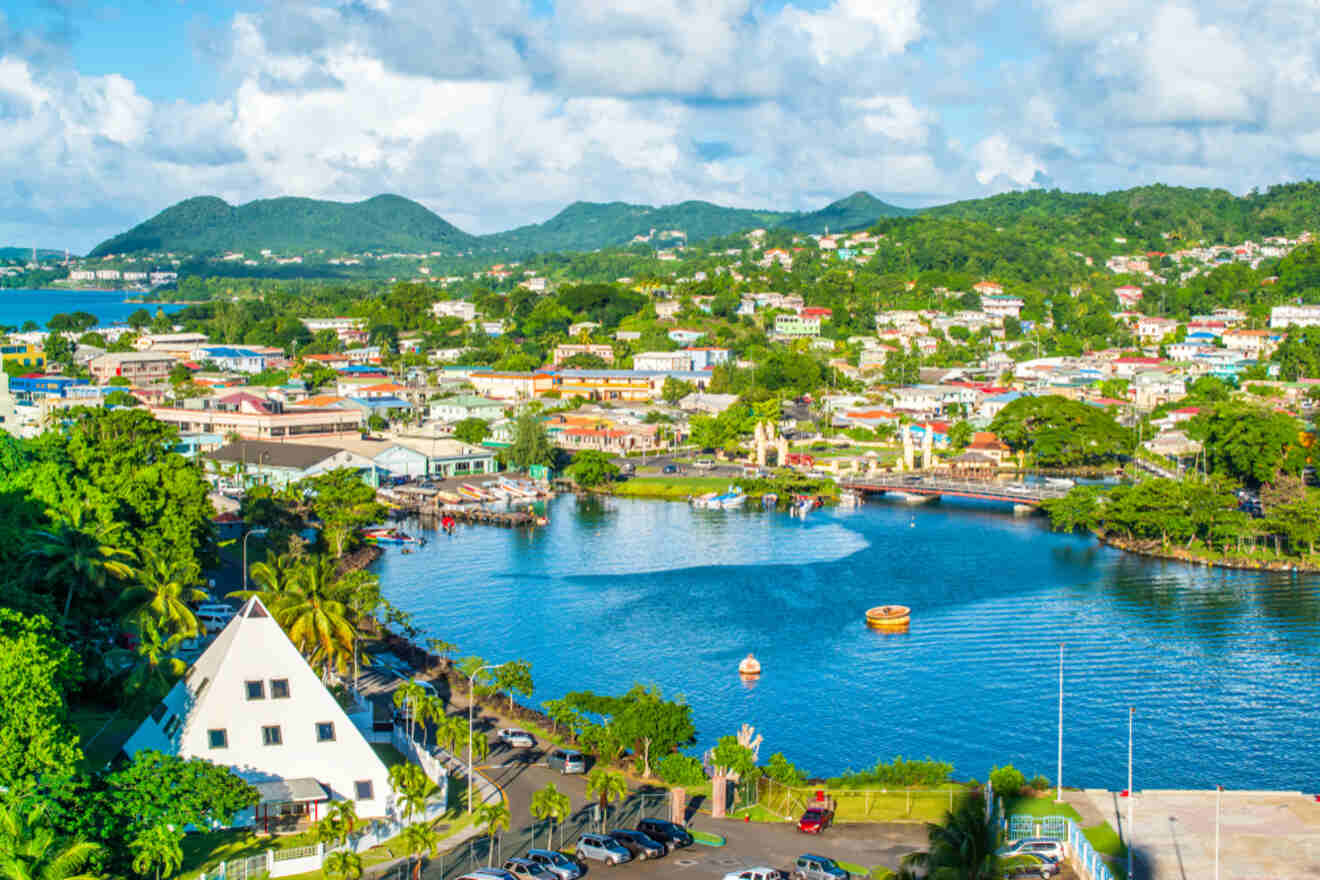 A vibrant aerial view of Castries, the capital of Saint Lucia, showcasing a mix of colorful buildings, a central bay, and surrounding green hills under a bright blue sky with scattered clouds.