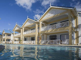 A two-story building with traditional architecture featuring intricate white railings, surrounded by a swimming pool with clear blue water.