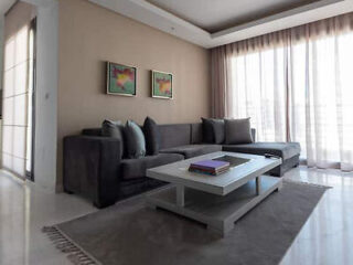 A modern living room with a dark grey sectional sofa, a coffee table, and large windows with sheer curtains.