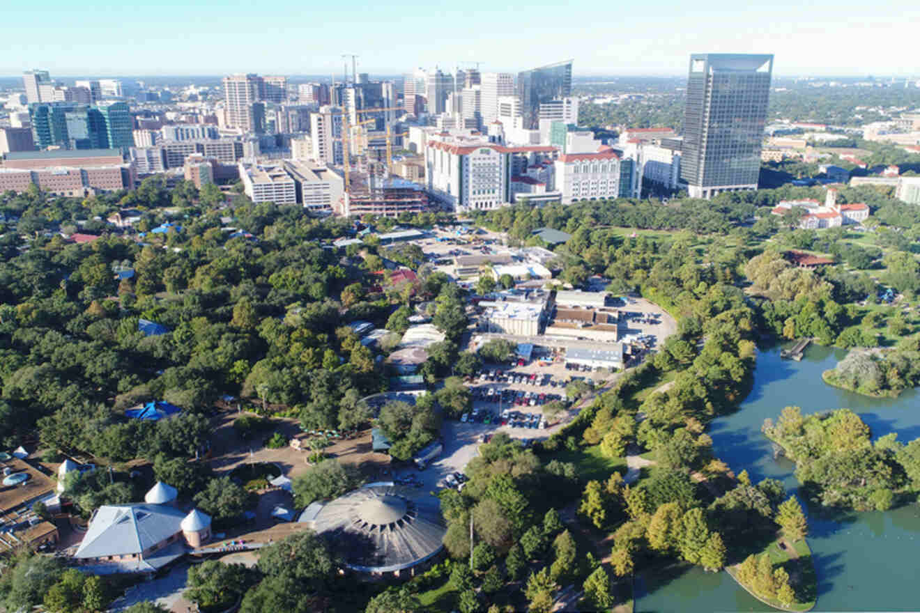 Aerial view of a cityscape featuring tall buildings, a lush green park with trees, and a river running through on a clear day.