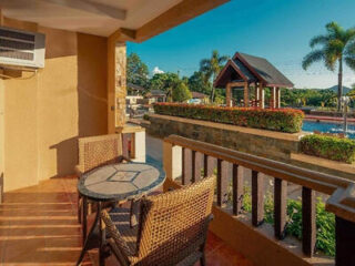 Private balcony at Coron Westown Resort, with a mosaic-topped table and rattan chairs overlooking the pool, thatched pavilion and palm trees.