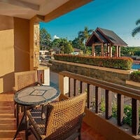 Outdoor patio with two wicker chairs and a round table overlooks a landscaped courtyard with a gazebo and greenery under a clear blue sky.