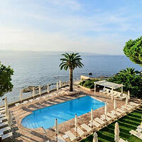 A serene view of a palm tree-lined pool overlooking the ocean at sunrise, with lounge chairs surrounding the pool