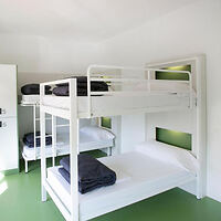 A clean, minimalist room with white walls and green flooring features white bunk beds each with folded black towels on top.