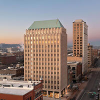 Aerial view of a cityscape featuring two prominent buildings with a clear sky at dusk. The taller building has a unique, pyramid-shaped roof.