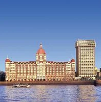 A large, historic building with a domed roof and adjacent modern high-rise standing by the waterfront, under a clear blue sky.