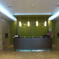 A modern reception desk in an office lobby with a green accent wall, overhead pendant lights, and a flower arrangement on the counter.