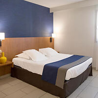 A cozy, modern hotel room featuring a neatly made king-size bed with white linens and a deep blue accent wall