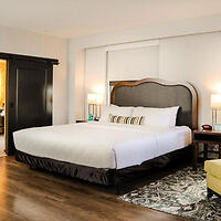 A hotel room with a king-sized bed, cushioned headboard, wooden floors, and a large sliding barn door 