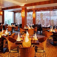 A well-lit restaurant interior with neatly arranged tables, chairs, and napkins. Large windows on the side provide a view of a cityscape.