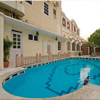 A serene outdoor swimming pool surrounded by a beige building with several windows and doors, featuring a geometric tile pattern at the bottom. A single white door is on the left wall.