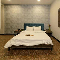 A neatly made bed with white linens, two pillows, and a blue upholstered headboard in a modern bedroom. There are side tables with lamps on either side and a book is placed on the bed.