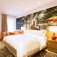 A modern hotel room with a large double bed, decorative wall art featuring a scenic street