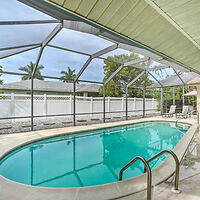 An enclosed outdoor swimming pool with metal railings and surrounding lounge chairs, under a screened structure with a view of trees and a fenced backyard.