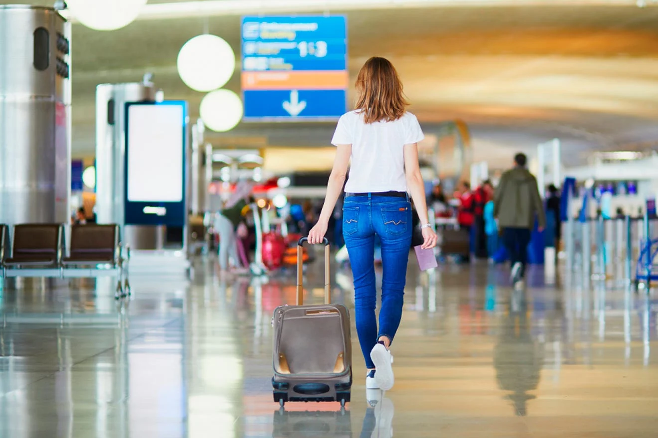 Person in casual attire, carrying a suitcase, walking through an airport terminal.