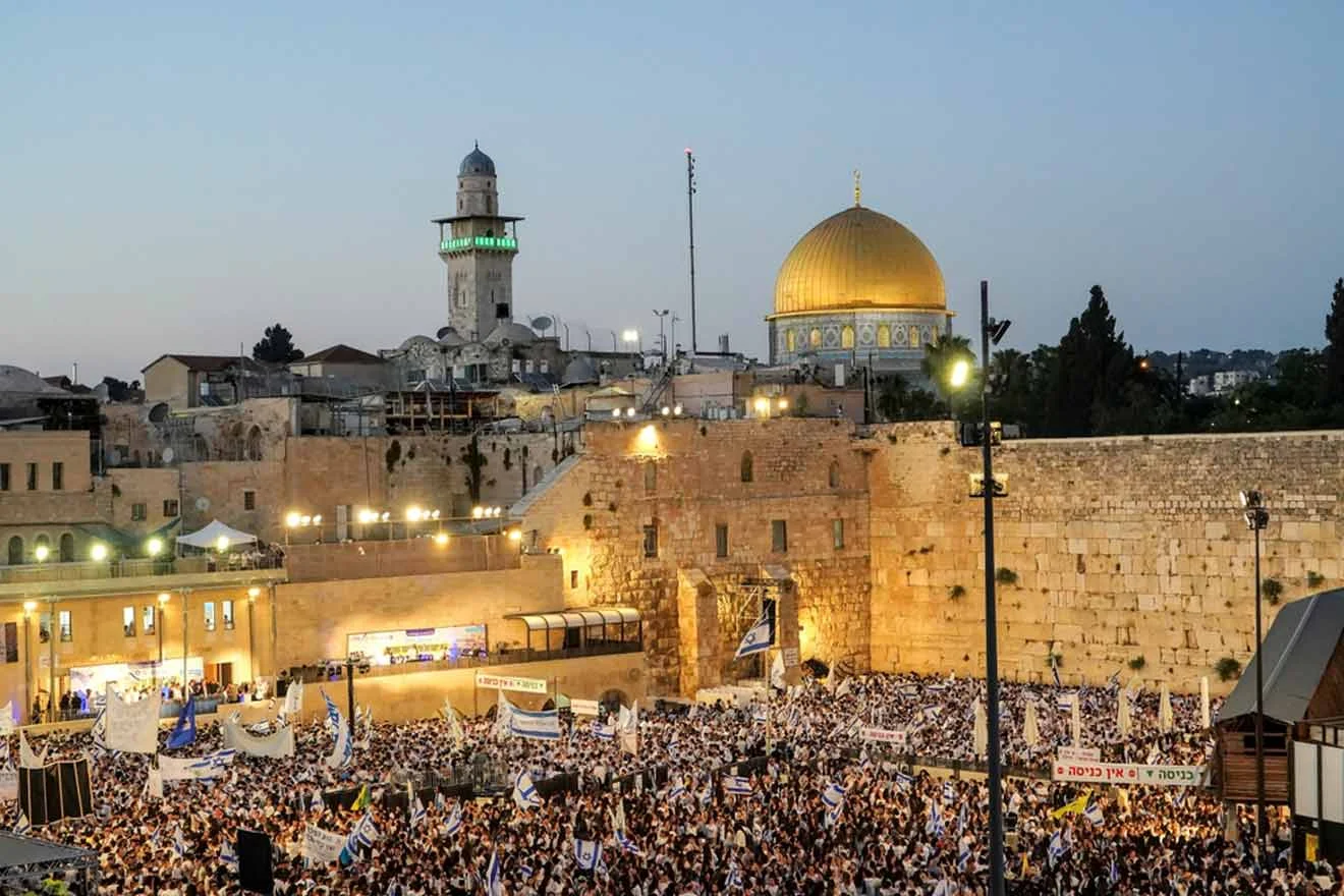 Crowd gathered in front of the Western Wall during an event, with the Dome of the Rock and other historical structures visible in the background at dusk.