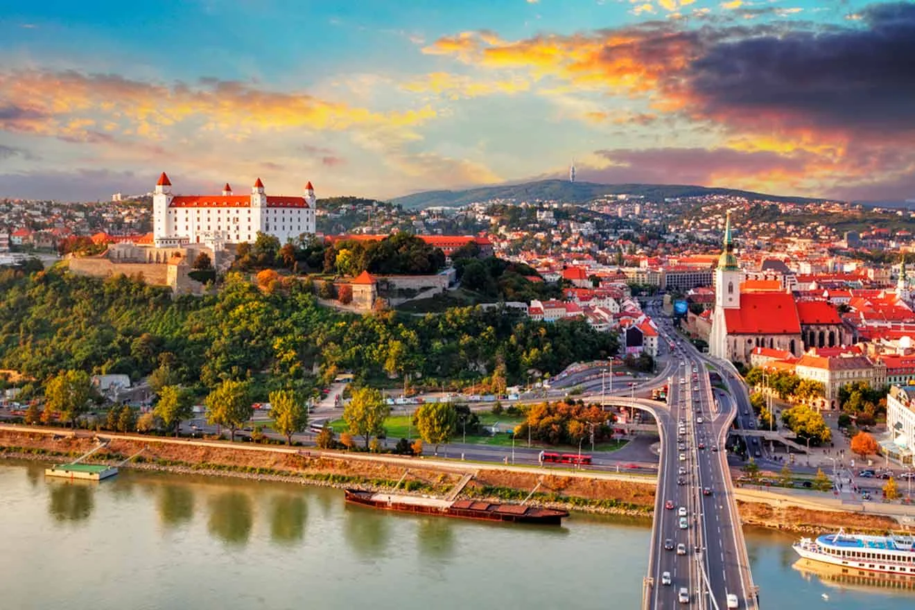 Aerial view of Bratislava, Slovakia, featuring the Bratislava Castle on a hill, the Danube River, and a bridge connecting the city.