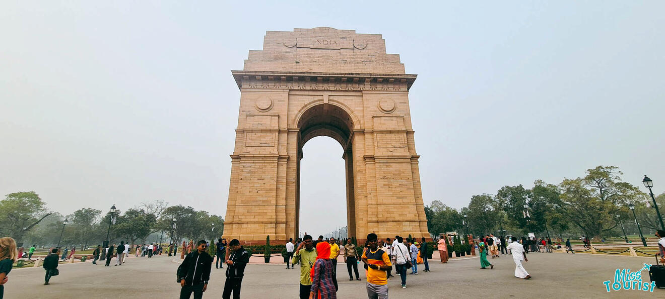 India Gate in Delhi, with people walking around the monument on a hazy day.