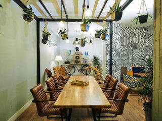 A modern meeting room features a wooden table with brown leather chairs, hanging plants, and geometric wall art.