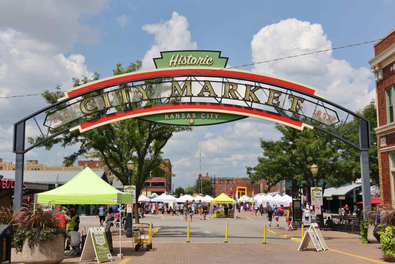 Entrance to the historic Kansas City City Market, with a large arch reading "City Market, Kansas City" and vendor stalls and tents in the background.