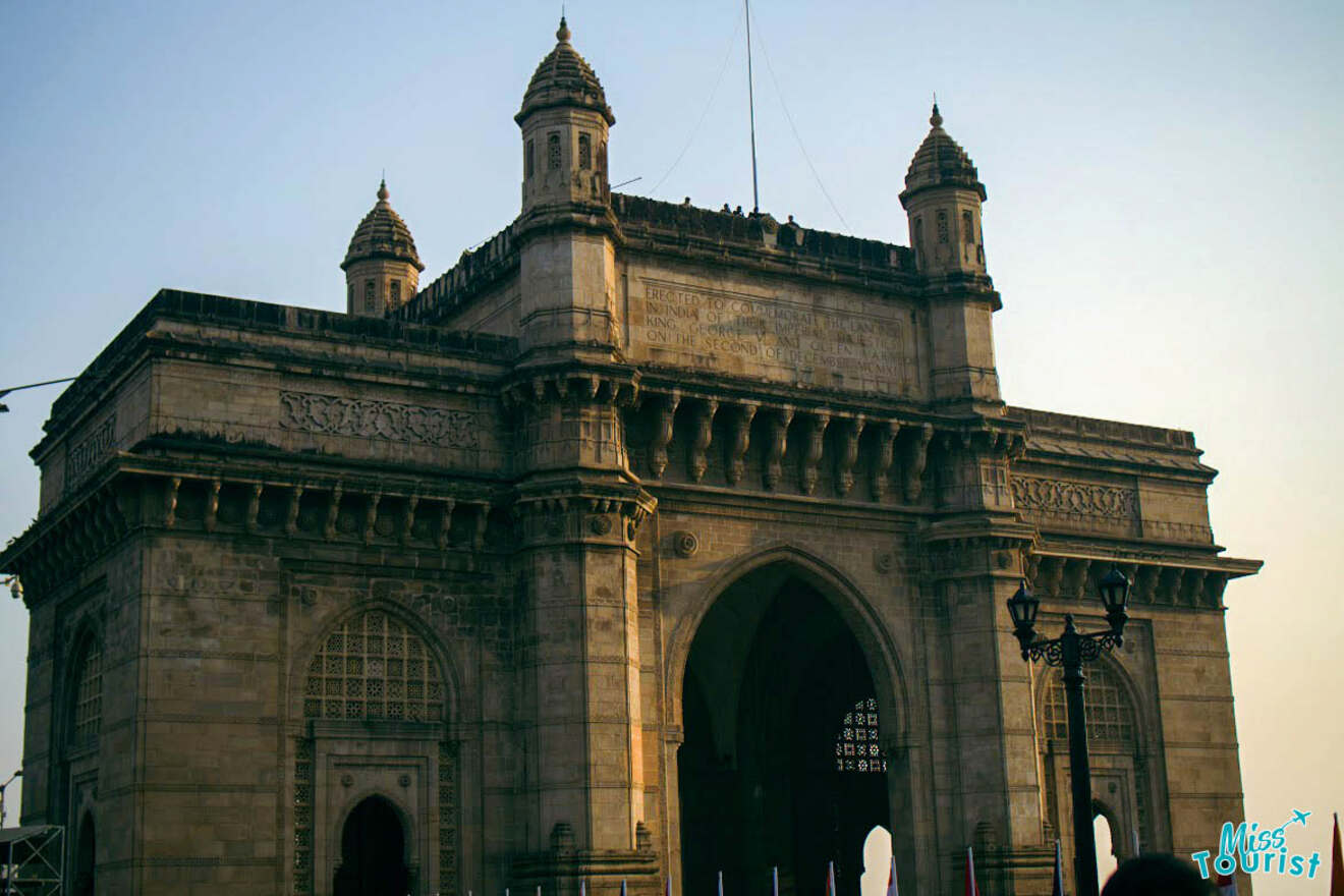 The image shows the Gateway of India, a monumental arch structure located in Mumbai, India, during daylight hours.