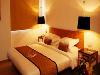 A cozy, well-lit hotel room with a large bed, hanging black lamps, and warm-toned decor.