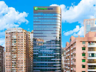 Exterior of the Holiday Inn Express, a modern glass building standing between older residential structures