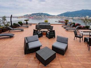 A rooftop terrace with modern gray seating, lounge chairs, and a panoramic view of the bay and distant mountains