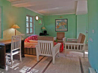 A spacious living room with pastel green walls, white wooden furniture, and natural light from windows.