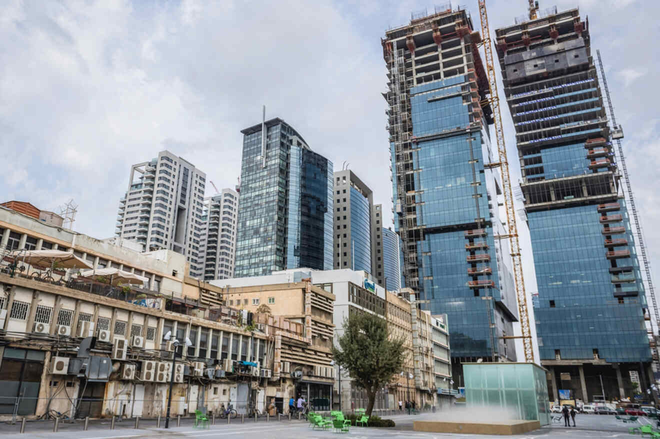 Tall modern skyscrapers under construction, with older, shorter buildings in front, featuring a contrast of architectural styles in Tel Aviv’s urban landscape.