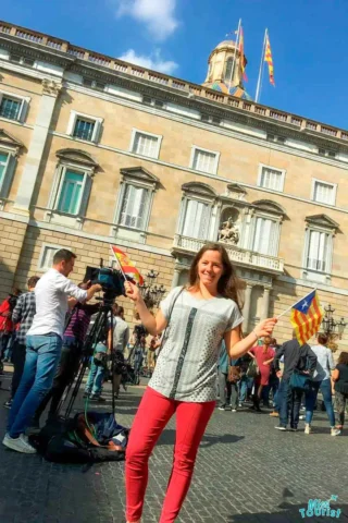 Darija Stojanovic, the author of the posts or misstourist, 
stands smiling in front of a historic building, holding two small flags. People and a camera setup are visible in the background.