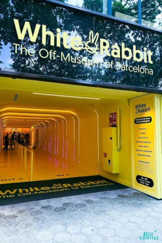 Entrance to the White Rabbit Museum in Barcelona, featuring a bright yellow tunnel and minimalist design. Signage displays the museum's name and tagline, "The Off-Museum of Barcelona.