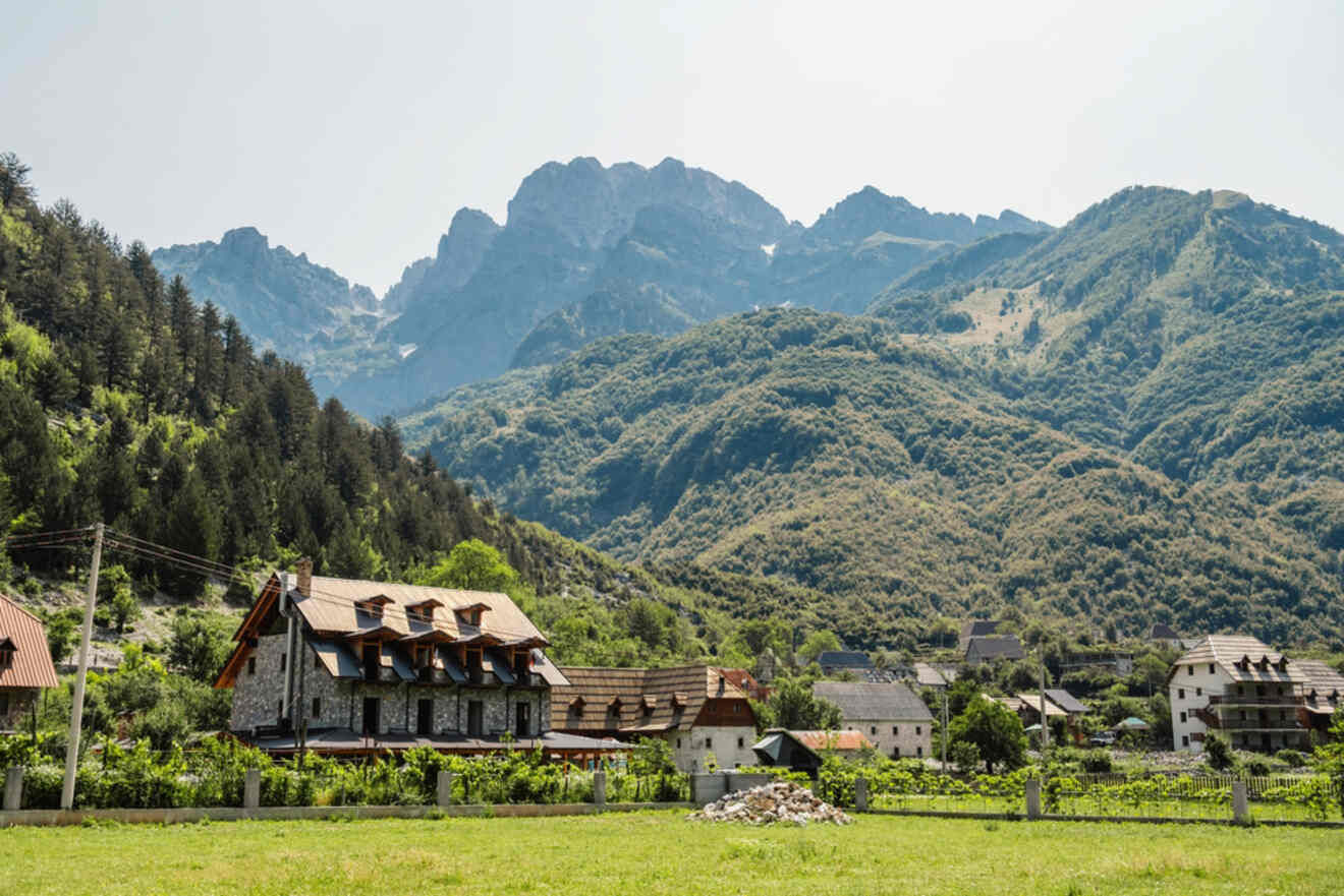 A picturesque view of a small village in Theth, Albania, surrounded by green fields and nestled against the backdrop of tall, rugged mountains.