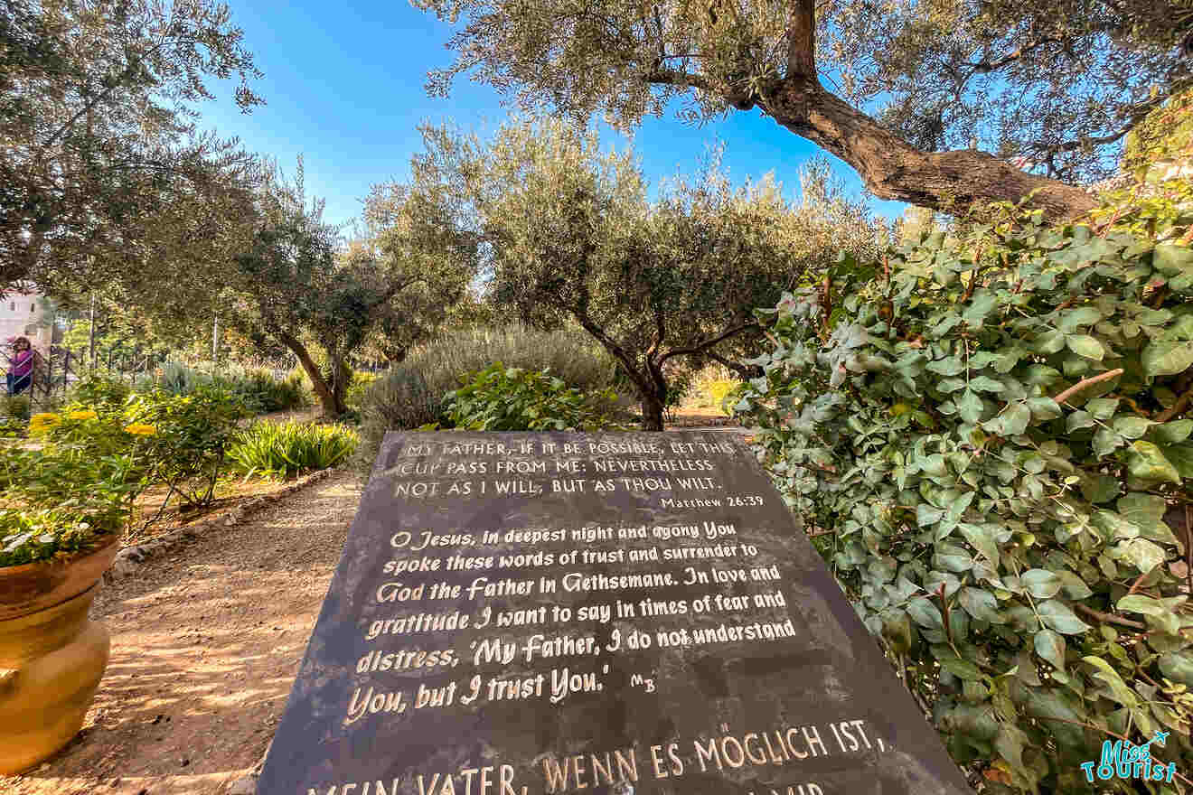 A stone tablet with religious inscriptions stands in a garden filled with lush greenery and trees.