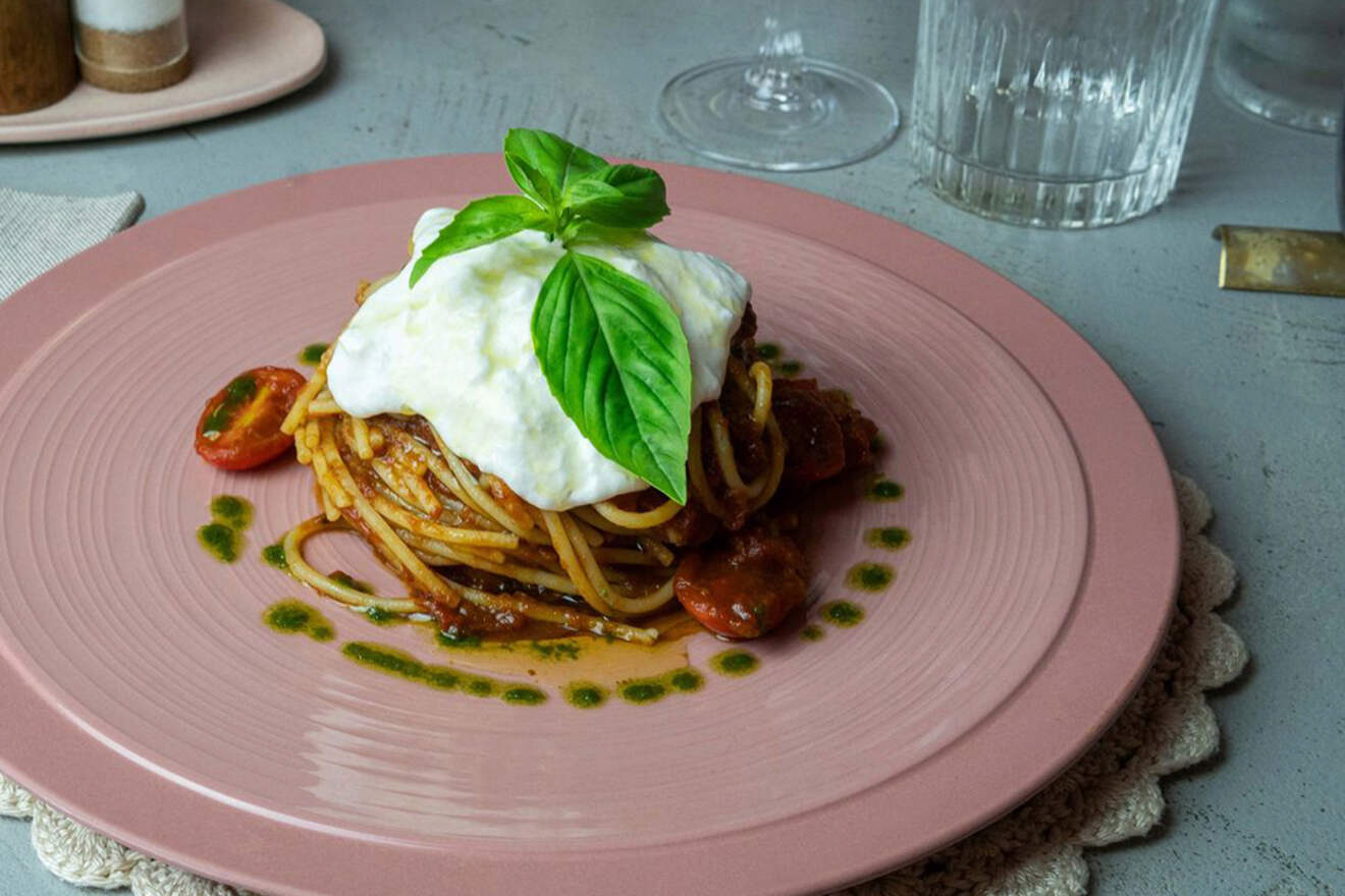 Spaghetti with tomato sauce topped with a dollop of mozzarella and fresh basil served on a pink plate, garnished with a green sauce ring.