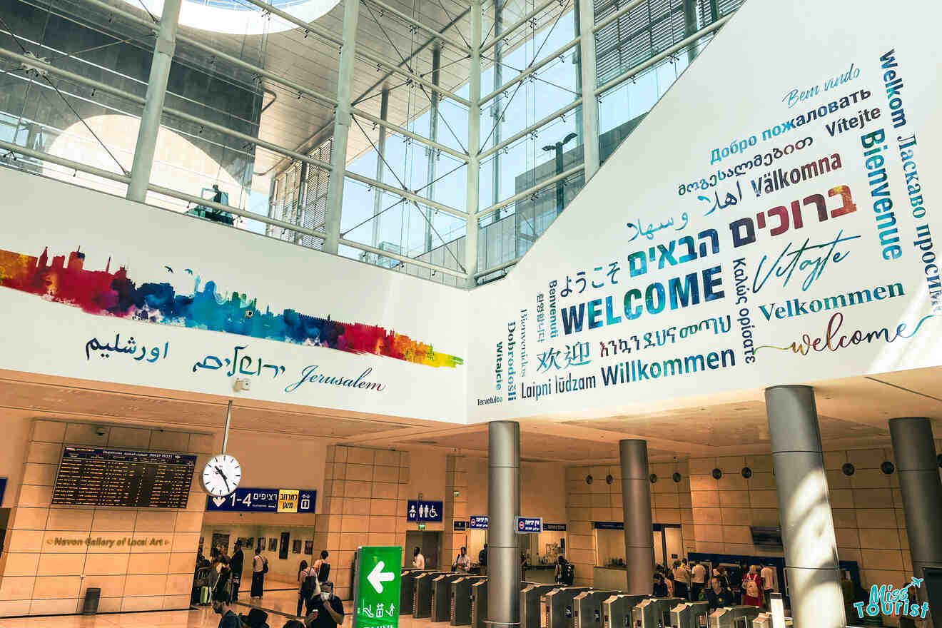 An airport terminal with a large "Welcome" sign in multiple languages on the wall, information displays, and people at the ticket gates and information desks.