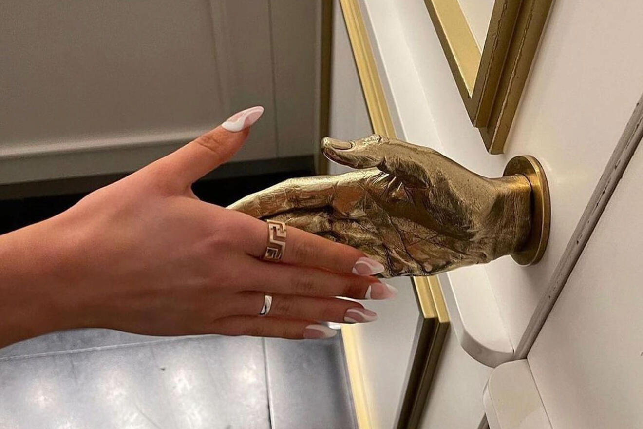 A close-up of a hand shaking hands with a golden hand-shaped door handle, set against a stylish and elegant background.