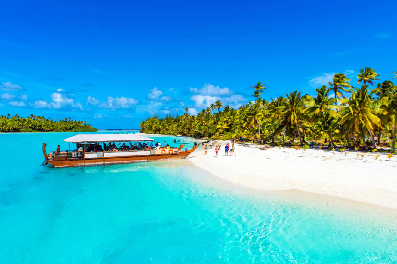 A traditional boat anchored near a white sandy beach with turquoise water and palm trees in Aitutaki, Cook Islands.